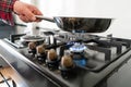 A man cooks in a frying pan, puts it on the stove. Modern gas burner and hob on a kitchen range. Dark black color and Royalty Free Stock Photo