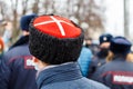 man in cossack hat with white cross on red watching blurry crowd of people