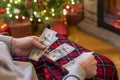 Man counting american dollars planning trip sitting near christmas tree and fireplace. Spending money on travel at christmas time.
