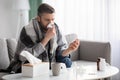 Man covered in blanket sneezing nose and checking for fever