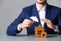 Man covering wooden houses with umbrella cutout at table, closeup.