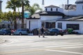 A man crossing a street wearing a black shirt and gray shorts surrounded by parked cars, lush green palm trees and buildings Royalty Free Stock Photo