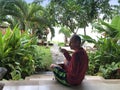 Man with a cup of coffee on the villaÃ¢â¬â¢s outdoor terrace has breakfast overlooking the pool and tropical plants. Indonesia, Bali