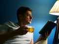 Man with cup of tea is reading book at evening. Royalty Free Stock Photo