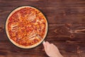 Man cuts the BBQ tasty pizza with ham, bbq sauce, bacon and salami, with a pizza cutter on a slate round platter which is on wood