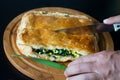 A man cuts with a knife, holding with the other hand, a homemade layer cake with green onions and eggs on a round wooden Board Royalty Free Stock Photo