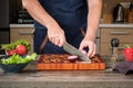 A man cuts onions on a beautiful wooden cutting board against the backdrop of a home kitchen Royalty Free Stock Photo