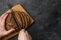 A man cuts a rustic bread with a knife on a cutting board on a dark background. Hands close up Royalty Free Stock Photo