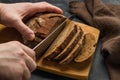 A man cuts a rustic bread with a knife on a cutting board on a dark background. Royalty Free Stock Photo