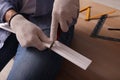 Man cutting foam crown molding with utility knife near wooden table, closeup Royalty Free Stock Photo