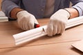 Man cutting foam crown molding with utility knife at wooden table, closeup Royalty Free Stock Photo