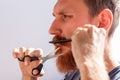 Man cutting his own beard and mustache with scissors and comb. Caucasian red bearded male trimming hair on face at home Royalty Free Stock Photo