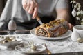 Man cutting poppy seed roll with knife. Festive table with poppy seed Easter cake, quail eggs, candles, spring branches. Royalty Free Stock Photo