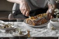 Man cutting poppy seed roll with knife. Festive table with poppy seed Easter cake, quail eggs, candles, spring branches. Royalty Free Stock Photo