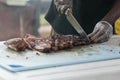 A man cutting up barbeque ribs from the smoker grill on cutting board with gloves on and a large knife. Royalty Free Stock Photo