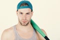 Man in cyan green baseball hat on white background. Guy in grey tank top holds bright green bat.