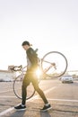 Man is a cyclist in dark sportswear, carrying a highway bike on his shoulders against the background of the sunset