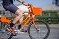 Male cyclist rides socially rented orange bicycle with basket on crossroad on city street