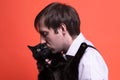 Man with dark hair and closed eyes holding and kissing muzzle cute black cat on coral background Royalty Free Stock Photo