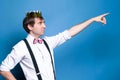 Man with dark hair in pink shirt, bow tie, suspender and gold shiny homemade crown pointing with finger to away