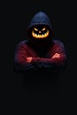 Man in dark hoodie with Jack-o`-lantern face glowing orange red, ominous looking