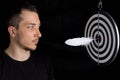 Man and dart board with a quill pen stuck in the center of the target on a black background in a low key Royalty Free Stock Photo