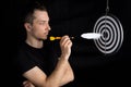 Man and dart board with a quill pen stuck in the center of the target on a black background in a low key Royalty Free Stock Photo