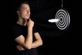 Man and dart board with a quill pen stuck in the center of the target on a black background in a low key Royalty Free Stock Photo