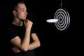 Man and dart board with a quill pen stuck in the center of the target on a black background in a low key Royalty Free Stock Photo