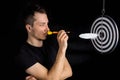 Man and dart board with a quill pen stuck in the center of the target on a black background in a low key Royalty Free Stock Photo