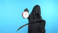 A man in a death suit with a scythe, shows a clock. blue background