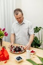 A man decorates a chocolate cake heart with fresh berries and chocolate icing. Present, surprise for