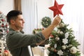 Man decorating Christmas tree with star topper indoors Royalty Free Stock Photo