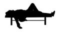 Man deeply sleeping or drunk, laying outdoors on a wooden park bench, silhouette.