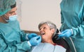 Man dentist operating senior woman in dental clinic