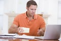 Man in dining room with laptop holding paperwork Royalty Free Stock Photo