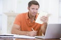 Man in dining room with laptop holding paperwork Royalty Free Stock Photo