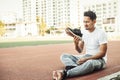 A man disgusted by the smell of his running shoe. A sport man sitting on the track race at stadium