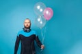 Man in diver suit making funny face and holding birthday balloons against blue studio wall banner background