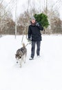 Man with dog on a leash walking in snowy pine forest in winter with Christmas tree in hands Royalty Free Stock Photo