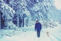 A man with a dog walks through a snowy pine forest Royalty Free Stock Photo