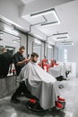 Man doing haircut in barber shop in modern light men`s hairdresser. Vertical photo of barber clipping client in chair. Client and