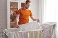 Man doing home chores. Caucasian man removes clothing and baby sheets after laundry from portable dryer in living room Royalty Free Stock Photo