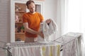 Man doing home chores. Caucasian man removes clothing and baby sheets after laundry from portable dryer in living room