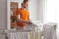 Man doing home chores. Caucasian man removes clothing and baby sheets after laundry from portable dryer in living room