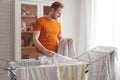 Man doing home chores. Caucasian man removes clothing and baby sheets after laundry from portable dryer in living room