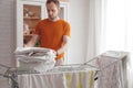 Man doing home chores. Caucasian man removes clothing and baby sheets after laundry from portable dryer in living room