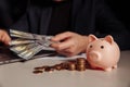 Man with dollar banknotes in his hand working using laptop, pink piggy bank with coins in front of him. Investment and Royalty Free Stock Photo