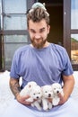 man with dreadlocks and beard holds puppies of four Japanese Spitz in his hands.