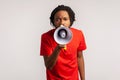 Man with dreadlocks wearing red casual style T-shirt, holding megaphone near mouth loudly speaking, screaming, making announcement Royalty Free Stock Photo